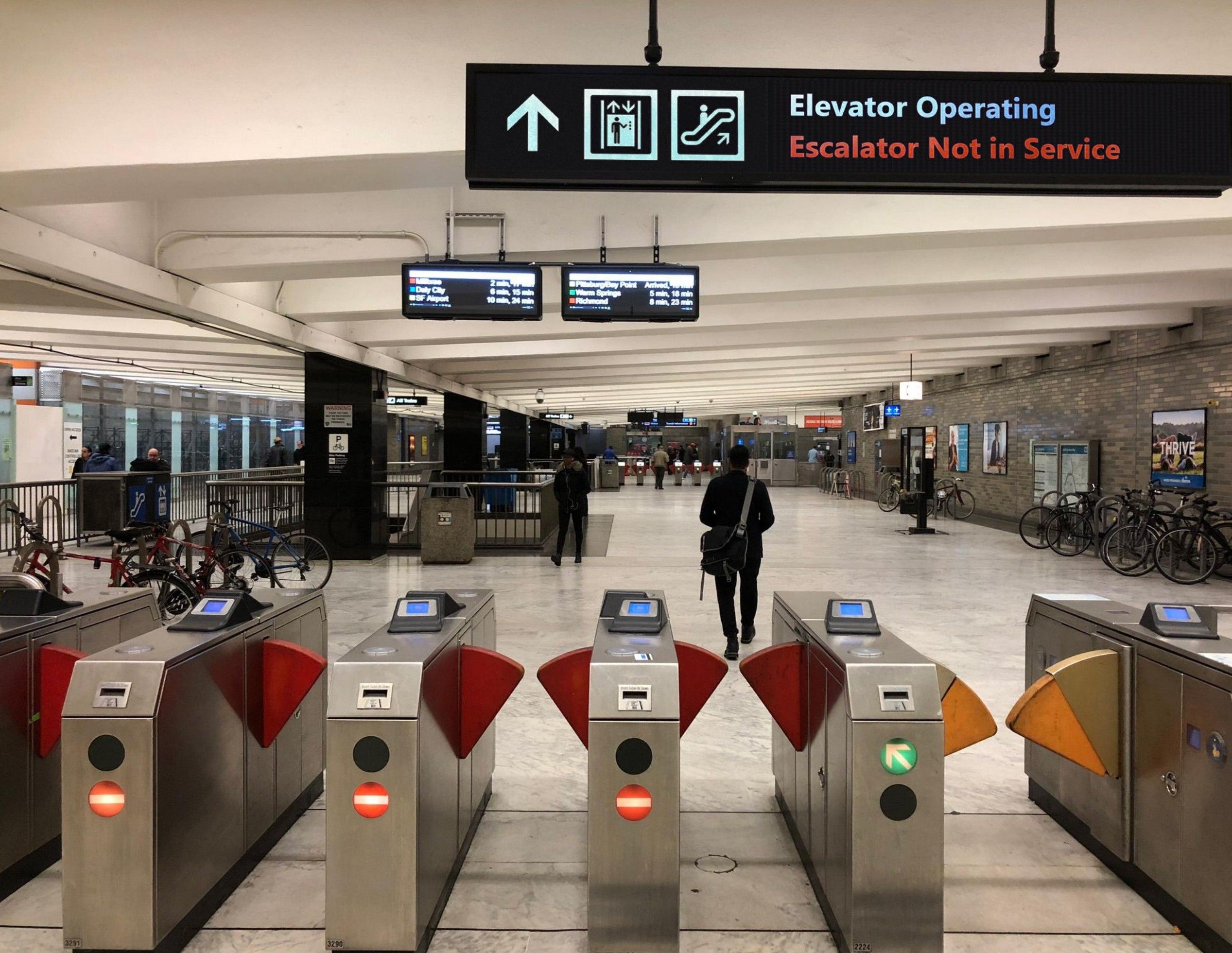 Station concourse and fare gates beneath an overhead elevator and escalator status sign